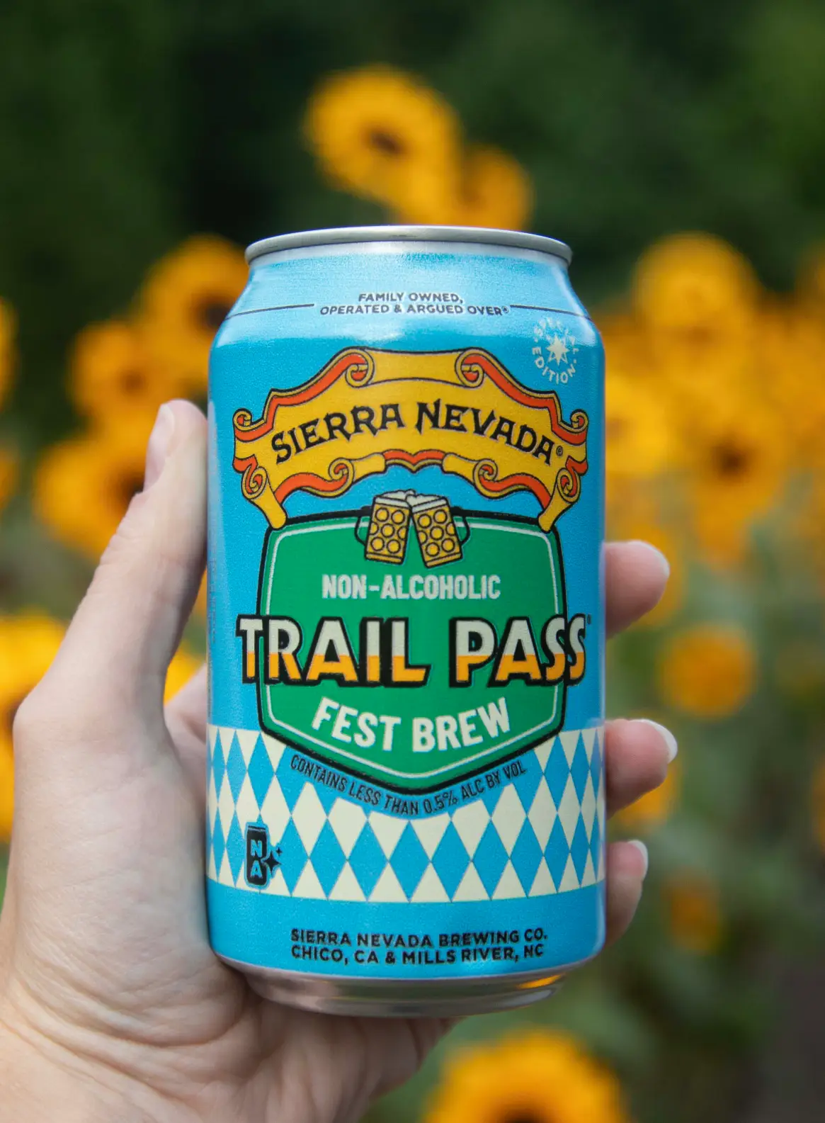Hand holding can of Trail Pass Fest Brew in front of flowers