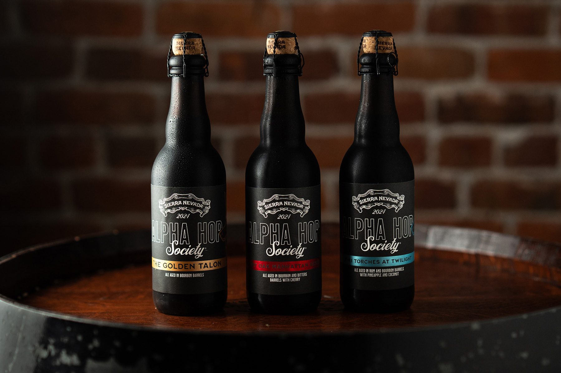 Three Alpha Hop Society beer bottles sitting on an oak barrel